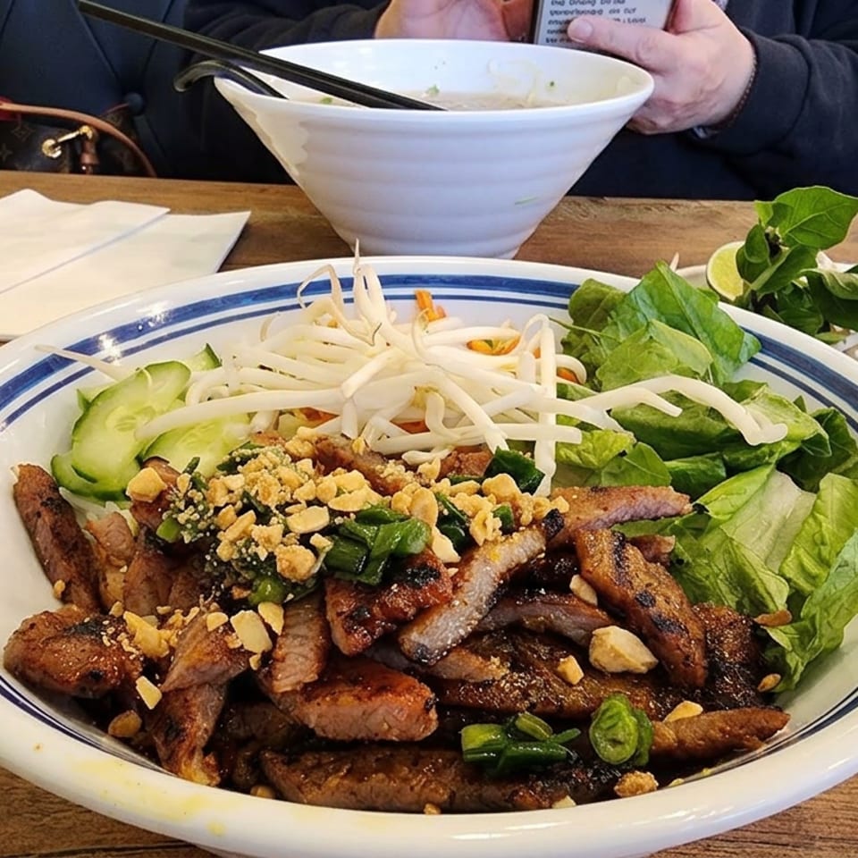 Vietnamese vermicelli bowl topped with grilled meat, lettuce, bean sprouts, cucumber, herbs, scallions, and crushed peanuts.